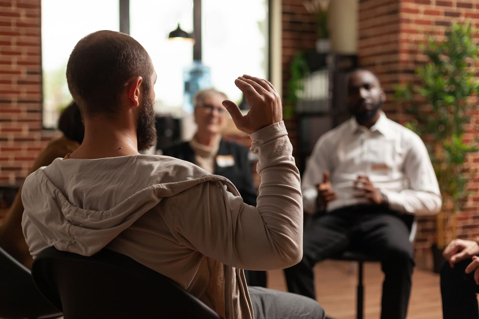 A support group of adults seated in a circle indoors, one speaking while others listen.